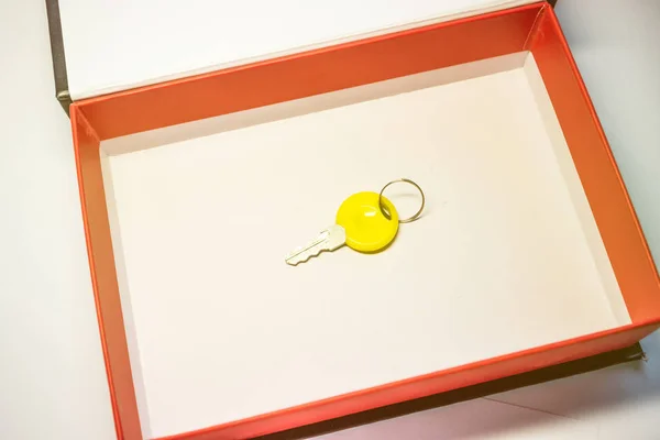 Una piccola chiave gialla in una scatola di cartone con bordo rosso — Foto Stock