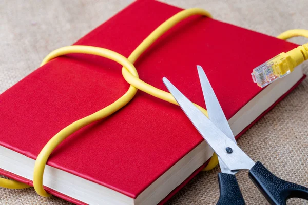 a red book is wrapped with an Internet cable. scissors are attached to it. scissors cut cable internet