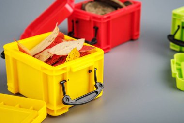 Gri arka planda sarı plastik bir kapta sonbahar yaprakları. Sikkeler ve yapraklar