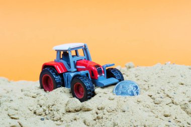 Kırmızı bir oyuncak, ruble sembollü bir bozuk paranın yanında traktörü kuma sürdü. Ruble yakında bir buldozer tarafından tırmıklanacak.
