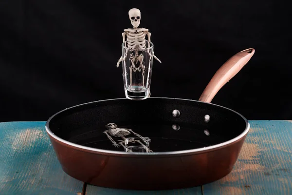 the skeleton is standing in front of the pan with a glass in the pan is another skeleton. bathing in hell