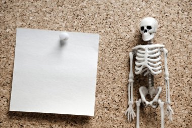 Çerçevenin sağ köşesindeki insan iskeleti mantar kaplamasına iliştirilmiş boş bir not kağıdıdır. kötü ya da mutsuz bir olayı bildirmek için