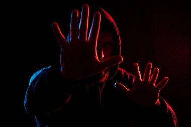 Farklı taraflardan koyu arkaplanlı bir adam mavi ve kırmızıyla farklı renklerde ışıklandırılmış. Büyü ya da korunma için kollarını aç