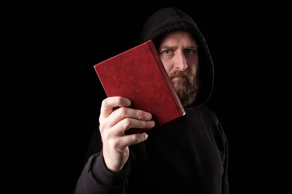 a bearded white man in a hood held a book in front of him. main book of humanity