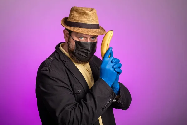 マスクと帽子の男は銃のようにバナナを手に持っている バナナキラー — ストック写真