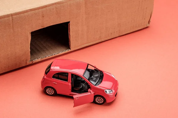 red toy car in front of a box in which a rectangular window is cut out, imitation of a garage. toy garage and auto