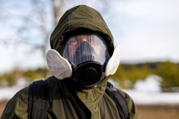 a man in a protective mask from gases looks into the frame against the background of nature. trip to the danger zone