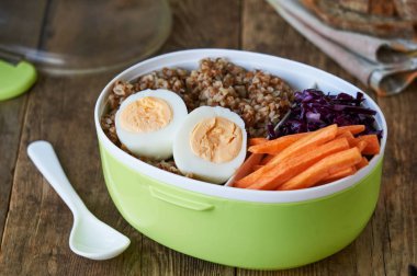 Ahşap masada Karabuğday, yumurta ve sebzeli öğle yemeği kutusu                               