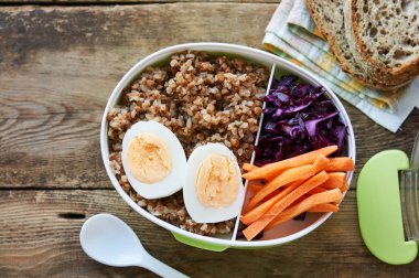 Ahşap masada Karabuğday, yumurta ve sebzeli öğle yemeği kutusu                               