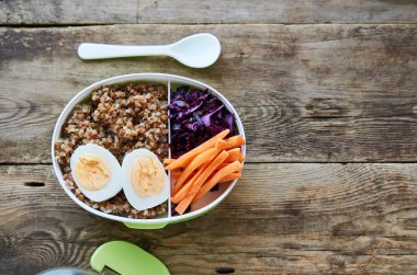 Ahşap masada Karabuğday, yumurta ve sebzeli öğle yemeği kutusu                               