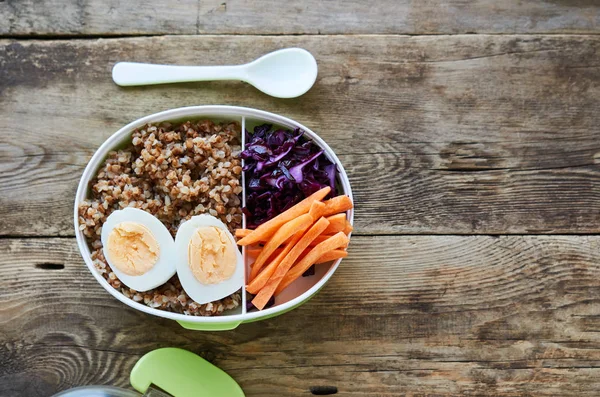 Ahşap masada Karabuğday, yumurta ve sebzeli öğle yemeği kutusu                               