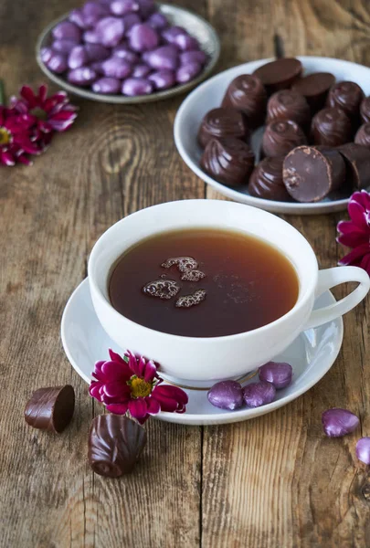 A cup of black tea with candies and flowers on a wooden table