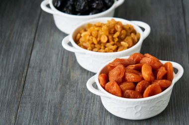 Ahşap arka planda beyaz kaselerde çeşitli kurutulmuş meyveler                               