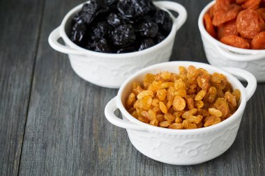 Ahşap arka planda beyaz kaselerde çeşitli kurutulmuş meyveler                               