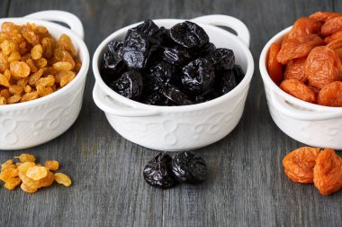 Ahşap arka planda beyaz kaselerde çeşitli kurutulmuş meyveler                               