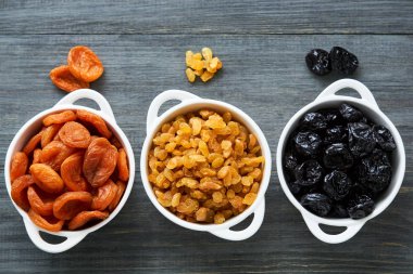 Ahşap arka planda beyaz kaselerde çeşitli kurutulmuş meyveler                               