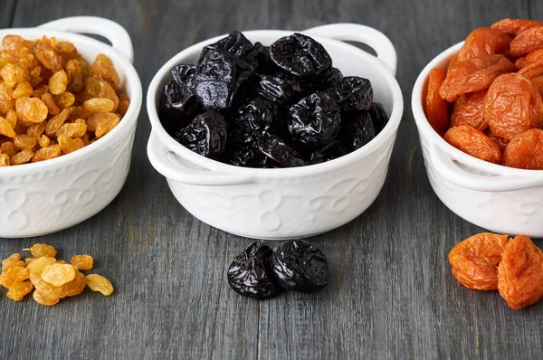 Ahşap arka planda beyaz kaselerde çeşitli kurutulmuş meyveler                               