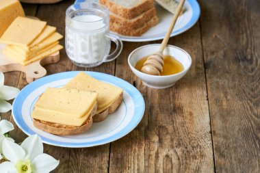 Ahşap bir masada peynirli sandviç, süt ve bal ile kahvaltı                               