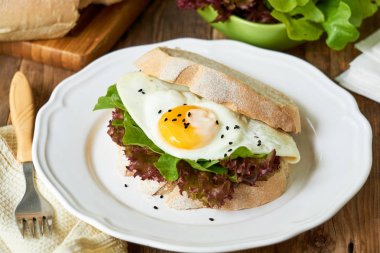 Beyaz bir tabak ta kızarmış yumurta ve marul yaprakları ile Sandviç                                