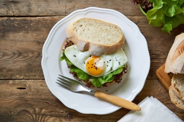 Beyaz bir tabak ta kızarmış yumurta ve marul yaprakları ile Sandviç                                