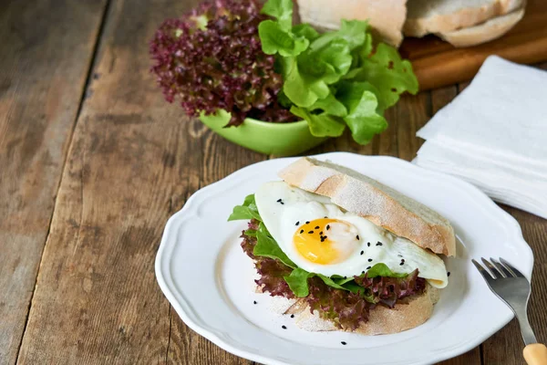 Beyaz bir tabak ta kızarmış yumurta ve marul yaprakları ile Sandviç                                