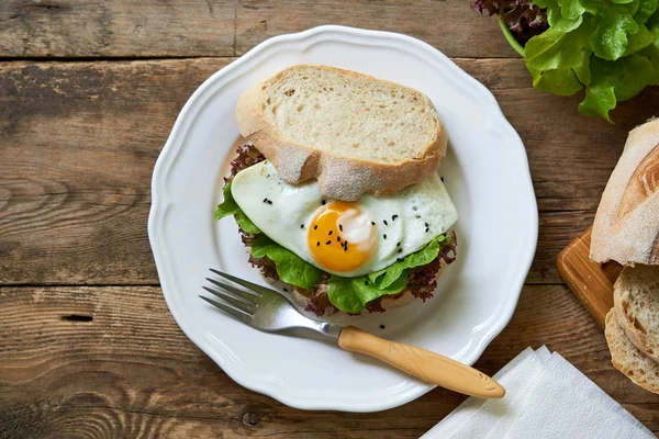 Beyaz bir tabak ta kızarmış yumurta ve marul yaprakları ile Sandviç                                