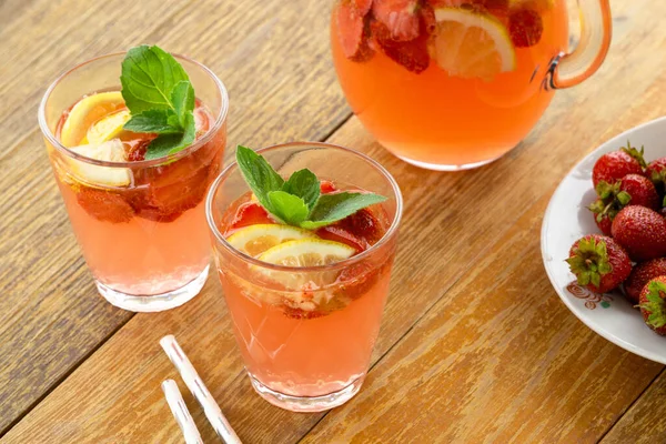 Summer pink lemonade with strawberries and mint in glasses on a wooden background