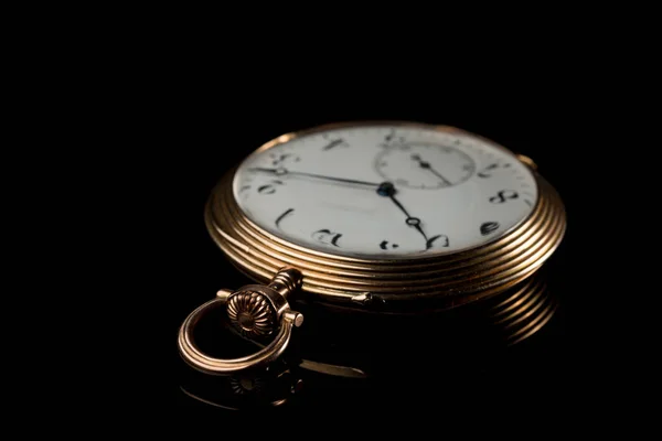 Closeup of an old, used golden pocket watch on a black reflective surface