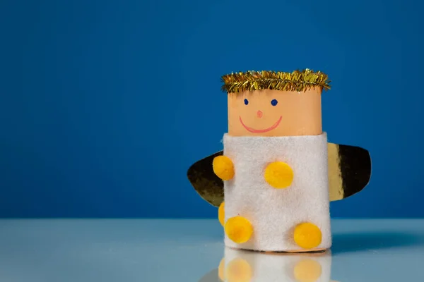 A small figure of an angel made of a toilet paper roll by a child, blue background — Stock Image Small Figure Angel Made Toilet Paper Roll Child Blue Background Stock Photo