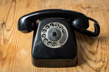 Tahta bir masanın üzerinde duran eski siyah bir telefon.