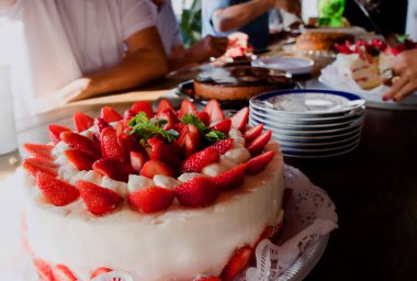 Çilekli pasta. Bir grup insan tatlı masasında oturuyor. Seçici odak.