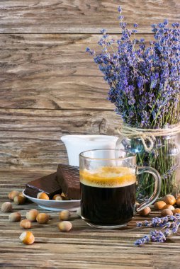 Dikey fotoğrafı yakın çekim: güzel kokulu siyah kahve çikolatalı kek, fındık, süt beyaz bir sürahi ve lavanta eski bir kaba ahşap arka plan üzerinde bir buket yanında bir bardak kupa