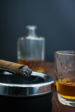 Bir kül tablası ve viski cam yakın çekim ve alkol arka plan ile bulanık bir sürahi için için yanan bir puro yakın çekim dikey fotoğraf