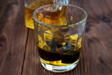 Bir cam bir kaba ahşap masa viski ve buz taş yakın çekim ile fotoğraf. Alkol arka plan dekoratif bir şişeyle parçası