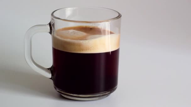 クレマの泡と新鮮な香り豊かなブラック コーヒーとガラスのマグカップにミルクを追加するクローズ アップ — ストック動画