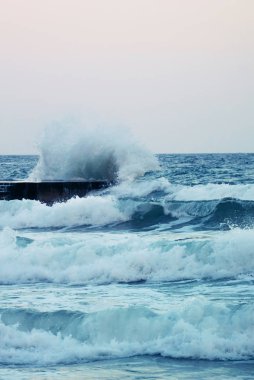Fırtınada beton iskelede kırılabilen mavi deniz dalgalarının dikey fotoğrafı