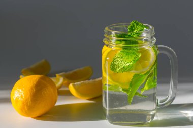Bir bardak dolusu su, dilimlenmiş limon ve nane yaprağı, bir dilim limon diliminin yanında.