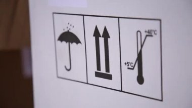 Bir karton kutu üzerinde işaretler. İşaretler kısıtlama sıcaklık ve nemden korumak ve bakım ürünleri ile temsil edilir. Beyaz renk kutu. İşaretleri siyah boya ile konur. Yakın çekim.