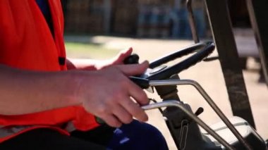 İşçi çatal yükleyici çalışır. Direksiyonu kontrol kolları büyük ölçüde kaldırılır. Çalışanın kısmen görülür. Ona tulum. Yüzsüz bir çekimde çalışanın olduğunu.