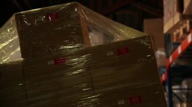 Çatal yükleyici bir depoda bir raf üzerinde paketlenmiş ürünler kaldırdı. Ürünler oluklu kutuları paketlenir. Ambalaj tarafından bir film düzenlenmiştir. Yakın çekim.