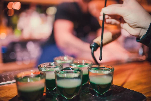 Líquido verde em vidros de tiro em pé no balcão. bartender saboreia coquetel usando uma palha — Fotografia de Stock