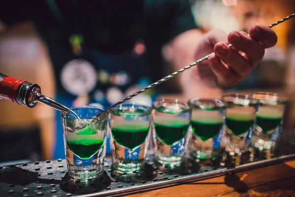 Green liquid in shot glasses standing on the counter. bartender preparing shots