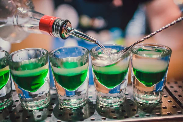 Green liquid in shot glasses standing on the counter. bartender preparing shots