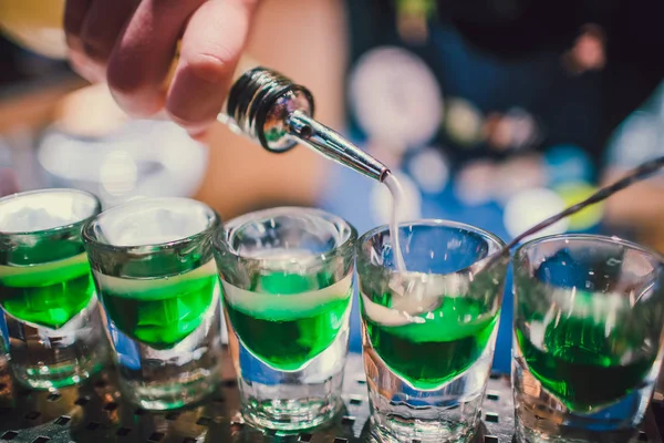 Green liquid in shot glasses standing on the counter. bartender preparing shots