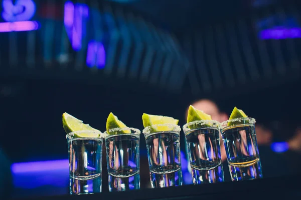 Tiros de tequila plateado con hielo y lima sobre fondo negro de mesa . — Foto de Stock