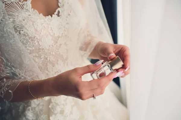 Sposa in un abito bianco con una manicure francese pastello tiene in mano una bottiglia di profumo . — Foto Stock