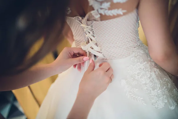 Demoiselle d'honneur attacher un arc sur une robe de mariée élégante mariée . — Photo