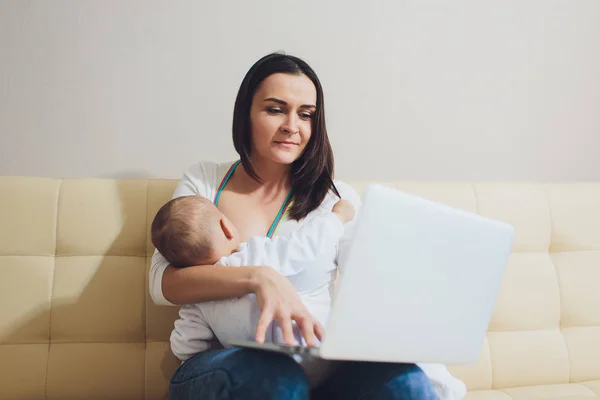 Hermosa madre joven que trabaja con computadora portátil y amamantando a su bebé recién nacido en casa. Mamá - mujer de negocios . —  Fotos de Stock