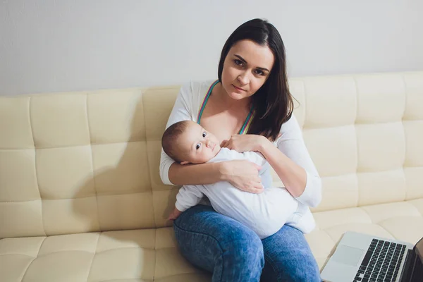 Hermosa madre joven que trabaja con computadora portátil y amamantando a su bebé recién nacido en casa. Mamá - mujer de negocios . —  Fotos de Stock