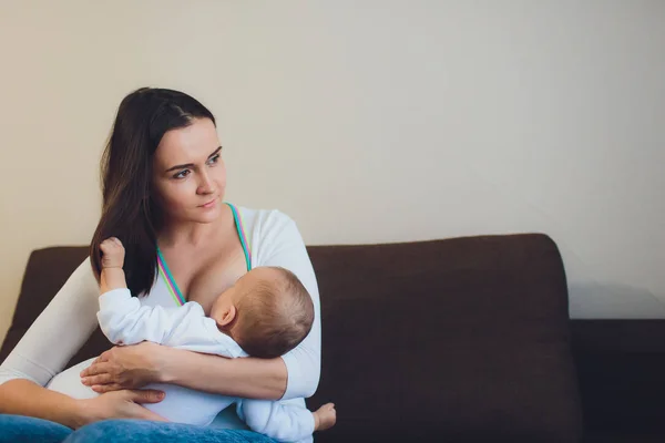 A Mother breastfeeding her little baby boy in her arms. brown sofa, home, white top — Stock Photo, Image